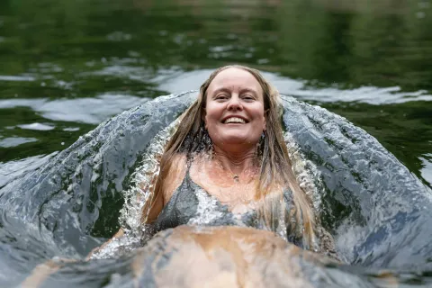 Åsa Mullaert badar i Odensjön med vågor som sköljer runt kroppen; blont hår och mörk baddräkt syns.