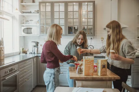 Tre personer står vid en köksö på Villa Söderåsens ljusa och vackra kök och skopar glass i strutar med förpackningar på bordet.