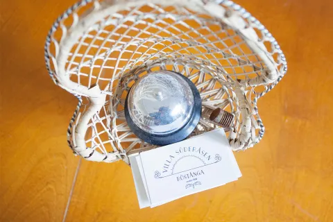 En flätad vit korg på ett träbord med en genomskinlig knapp och ett visitkort som ligger ovanpå.