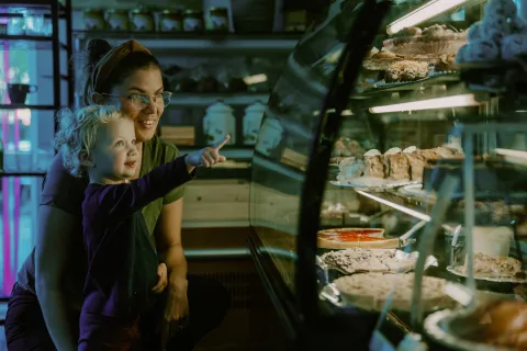 Ett barn pekar på bakverk i en upplyst glasmonter på Cafe Fenix i Röstånga, medan en vuxen sitter bredvid.