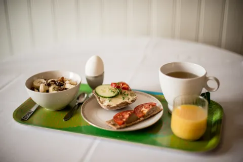 En frukostbricka på Villa Söderåsen med skål müsli, kokt ägg, smörgåsar med grönsaker, kopp te och glas apelsinjuice.