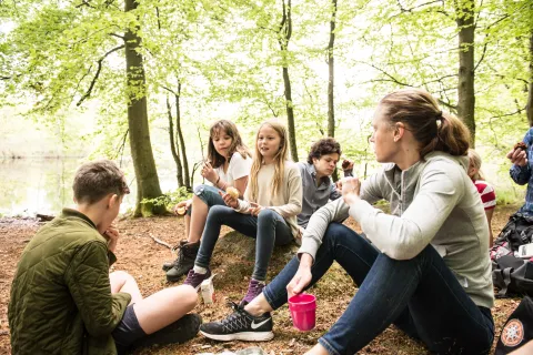 En grupp ungdomar sitter på marken i en skogsglänta i nära Härsnäsdammarna i Söderåsens Nationalpark och tar en paus med snacks och dryck.